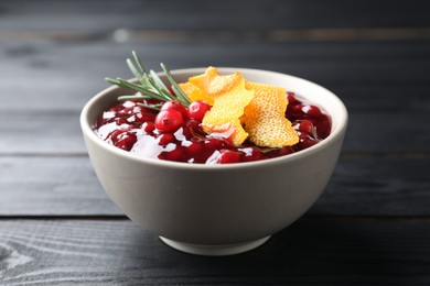 Photo of Fresh cranberry sauce, rosemary and orange peel in bowl on black wooden table, closeup