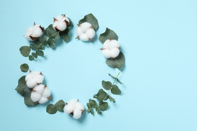 Frame of cotton flowers and eucalyptus leaves on light blue background, flat lay. Space for text