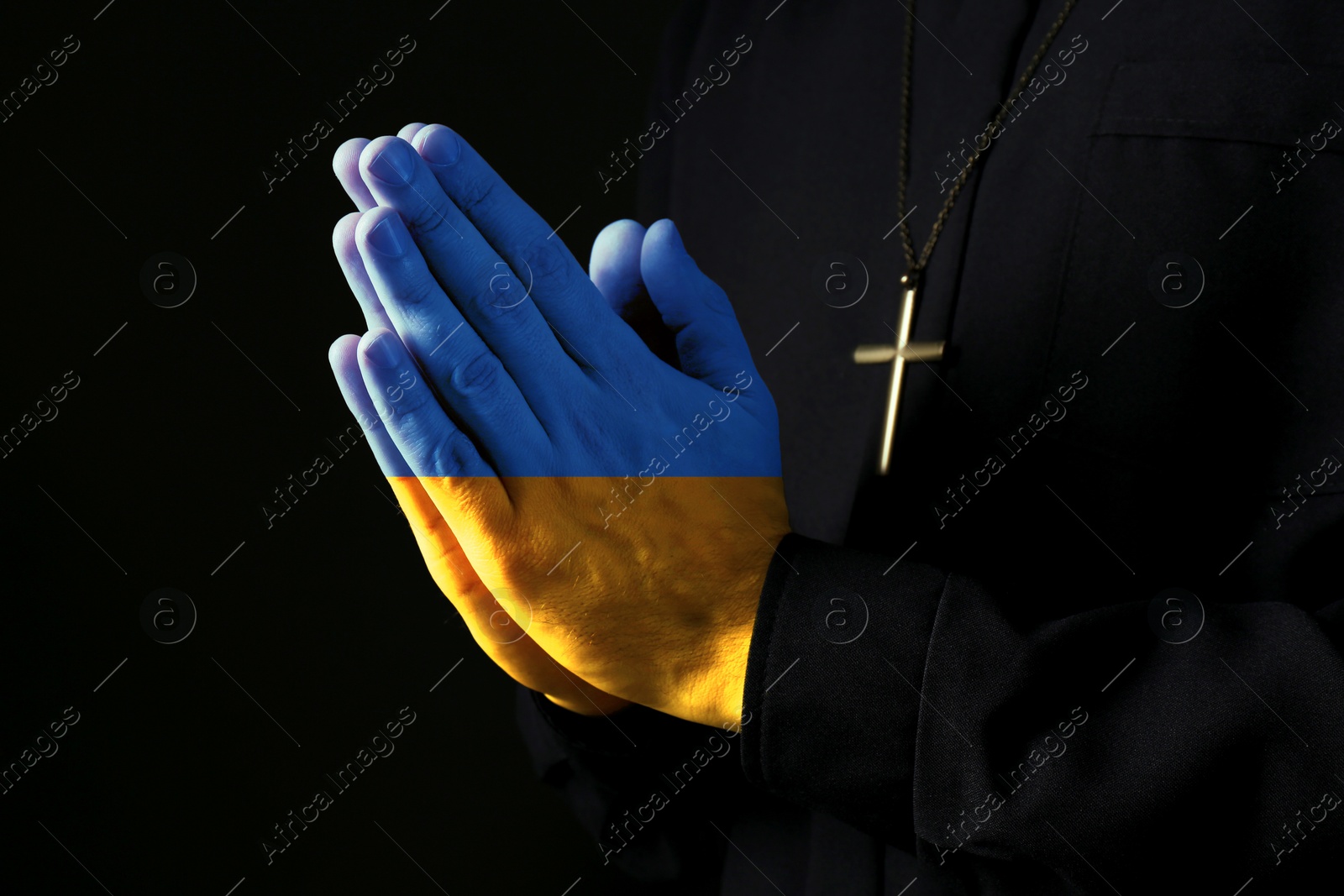 Image of Pray for Ukraine. Priest on dark background, closeup. Hands toned in colors of Ukrainian flag