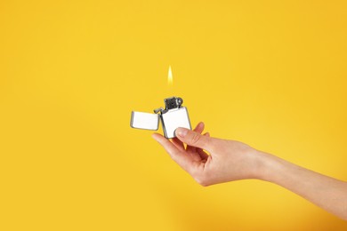 Photo of Woman holding lighter with burning flame on orange background, closeup