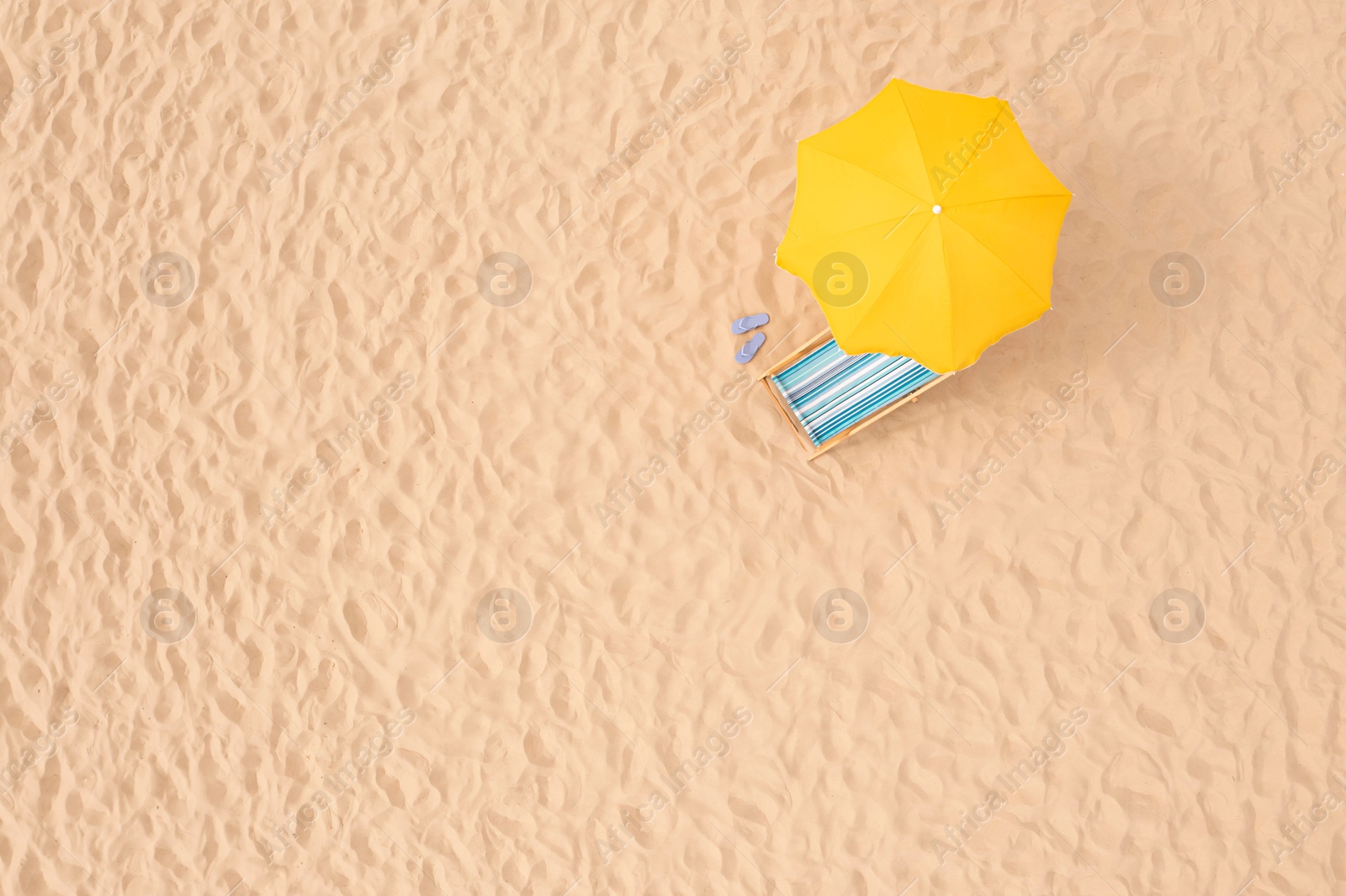 Image of Yellow beach umbrella, sunbed and flip flops on sandy coast, aerial view. Space for text