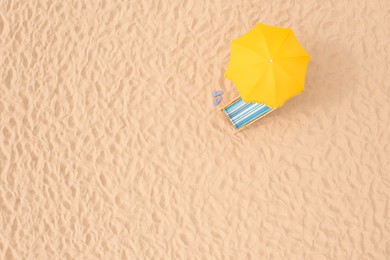 Yellow beach umbrella, sunbed and flip flops on sandy coast, aerial view. Space for text