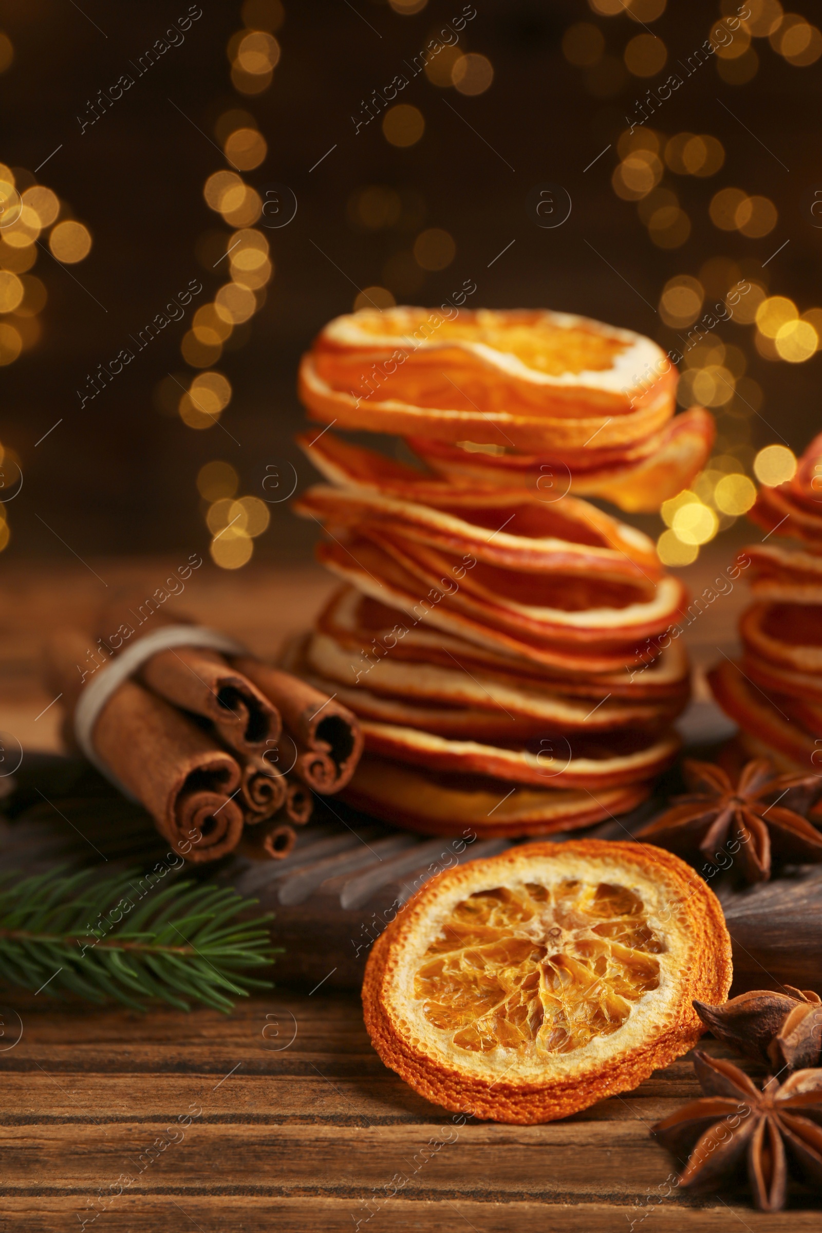 Photo of Dry orange slices, anise stars and cinnamon sticks on wooden table. Bokeh effect