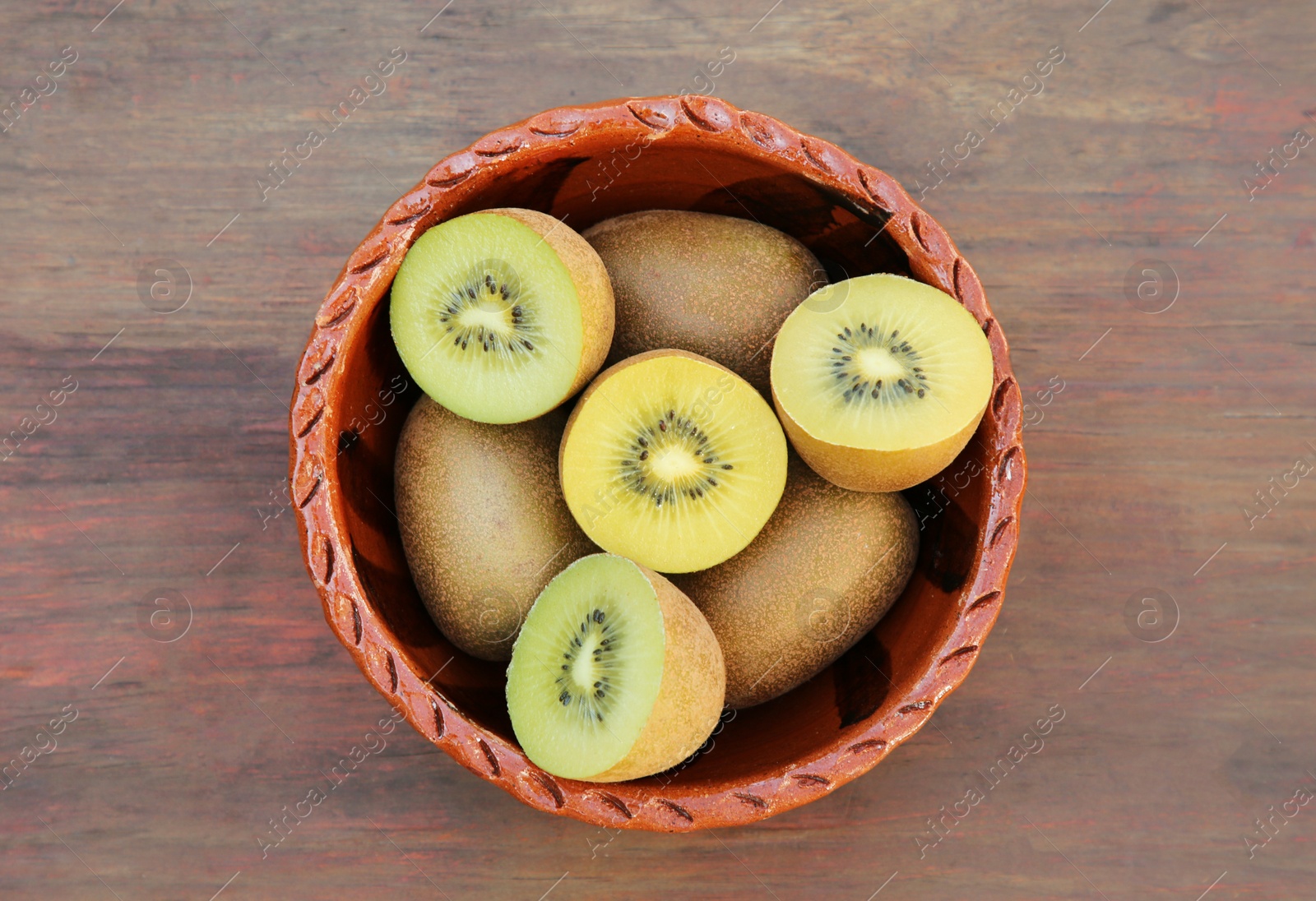 Photo of Bowl with many whole and cut fresh kiwis on wooden table, top view