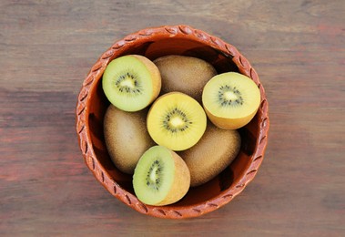 Photo of Bowl with many whole and cut fresh kiwis on wooden table, top view