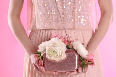 Photo of Woman holding elegant handbag with spring flowers on pink background, closeup