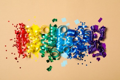 Photo of Colorful serpentine streamers and confetti on beige background, flat lay