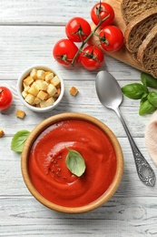 Photo of Fresh homemade tomato soup served with bread and croutons on white wooden table, top view