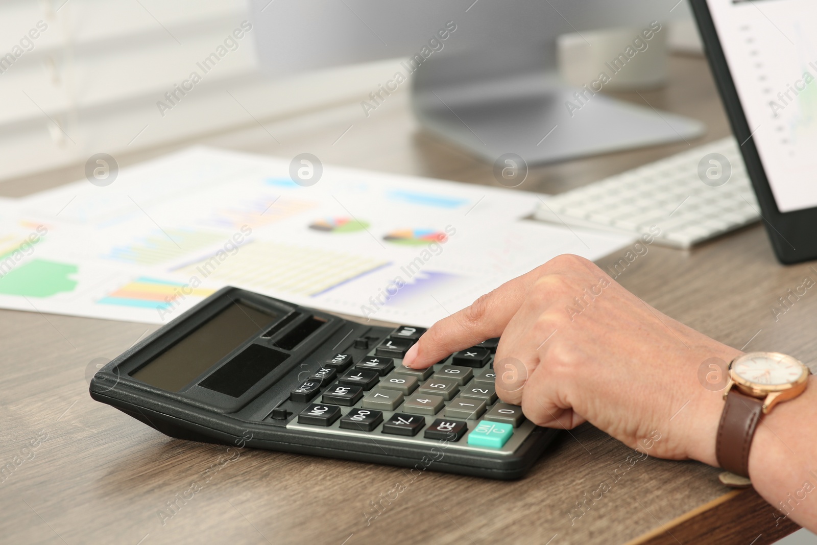 Photo of Accountant using calculator at wooden desk in office, closeup