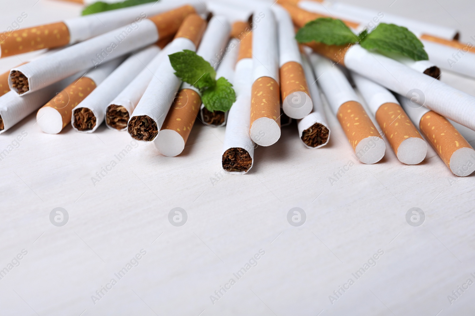 Photo of Menthol cigarettes and mint on white wooden table. Space for text