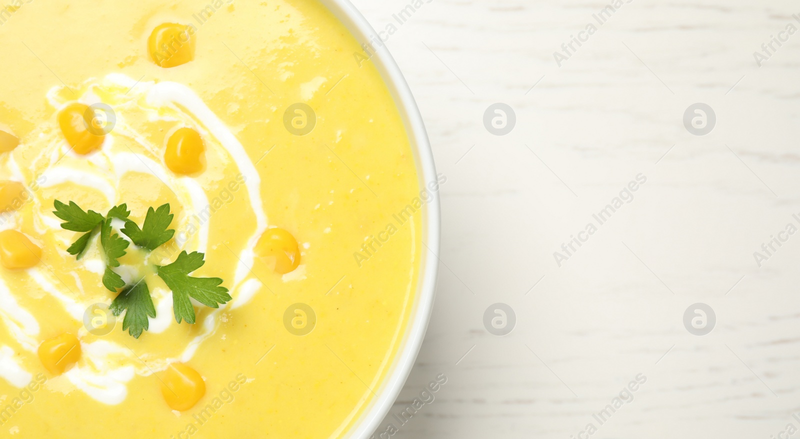 Photo of Delicious creamy corn soup served on white wooden table, top view. Space for text