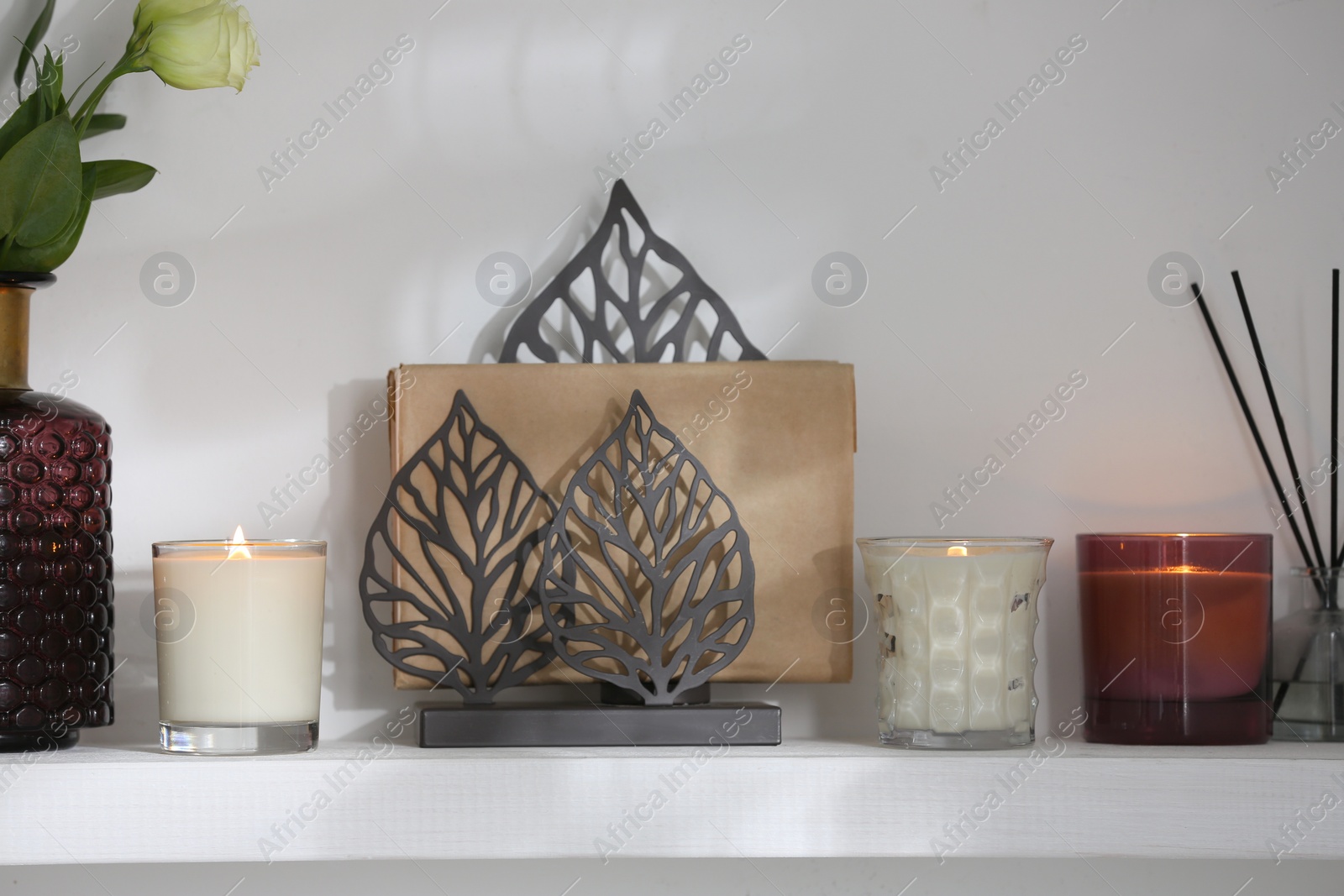 Photo of Burning candles. flowers and decor on white shelf