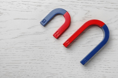 Photo of Red and blue horseshoe magnets on wooden background, top view with space for text
