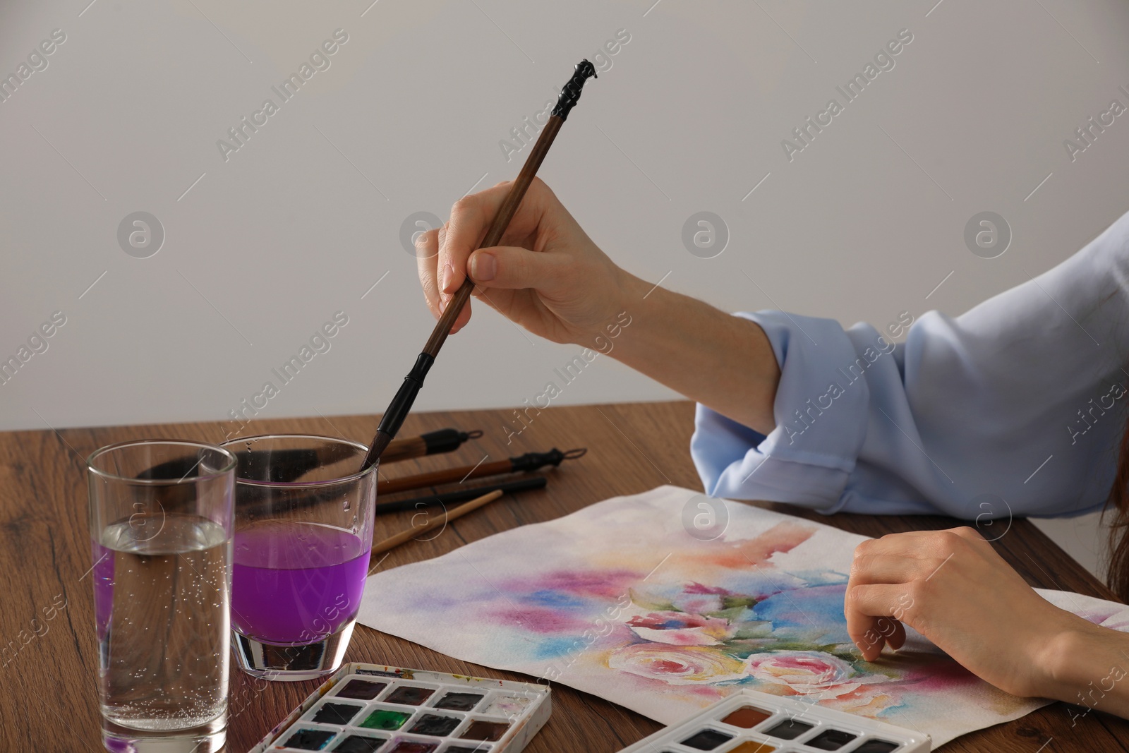 Photo of Woman painting flowers with watercolor at wooden table indoors, closeup. Creative artwork