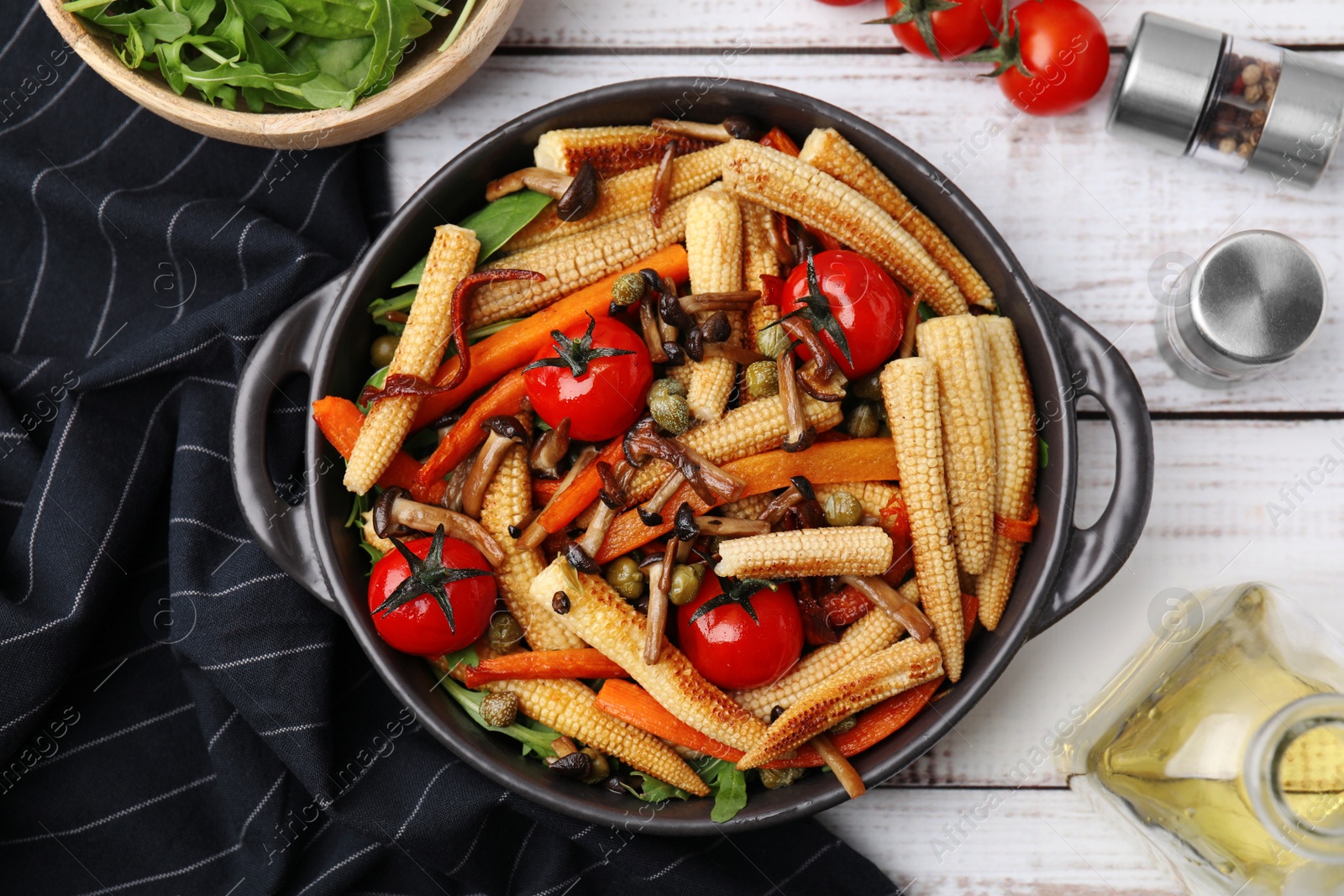 Photo of Tasty roasted baby corn with tomatoes, capers and mushrooms on white wooden table, flat lay