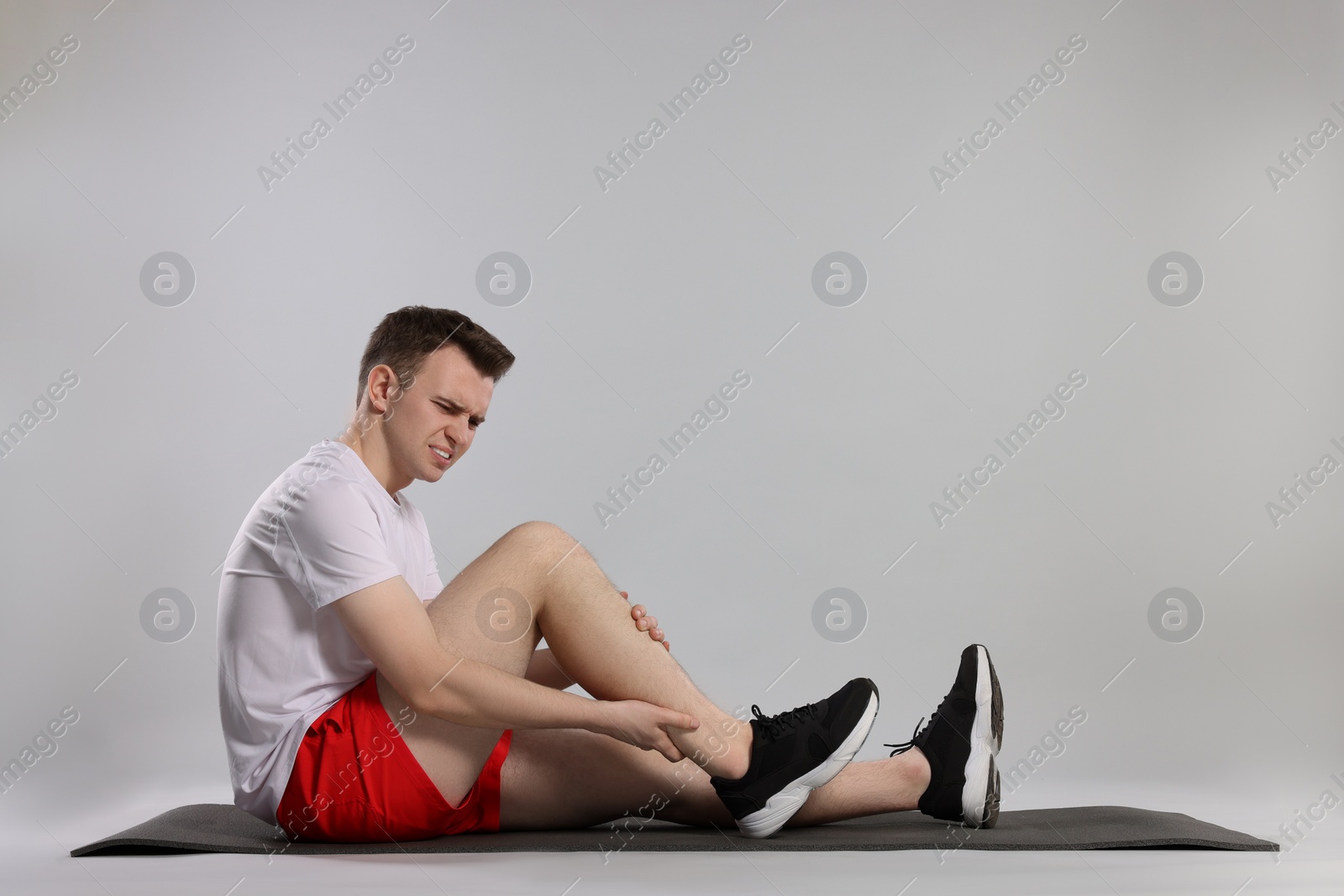 Photo of Man suffering from leg pain on mat against grey background