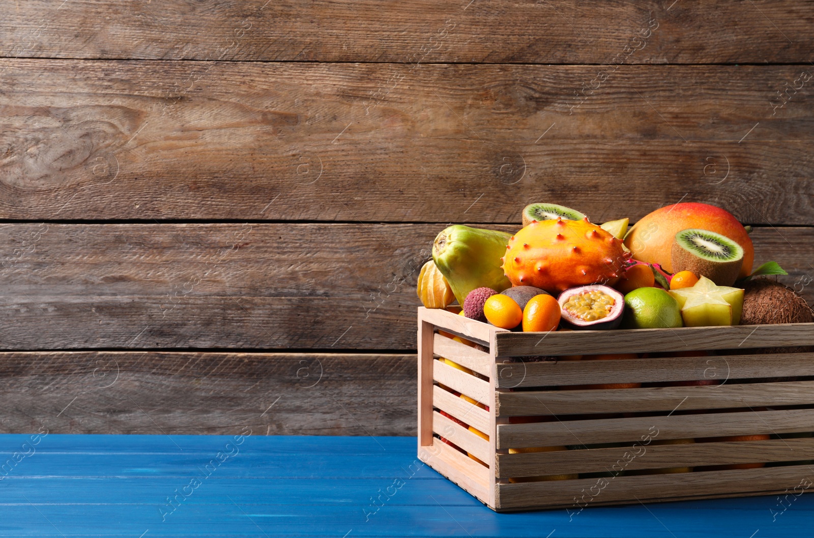 Photo of Crate with different exotic fruits on blue wooden table. Space for text