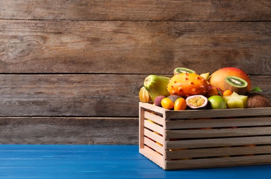 Photo of Crate with different exotic fruits on blue wooden table. Space for text