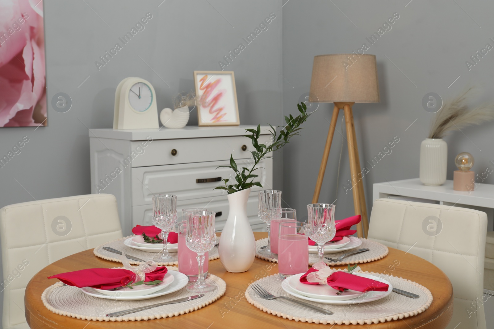 Photo of Color accent table setting. Glasses, plates, vase with green branch and pink napkins in dining room