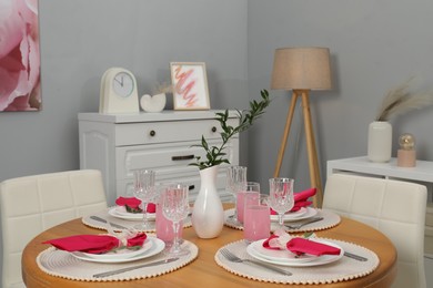 Color accent table setting. Glasses, plates, vase with green branch and pink napkins in dining room