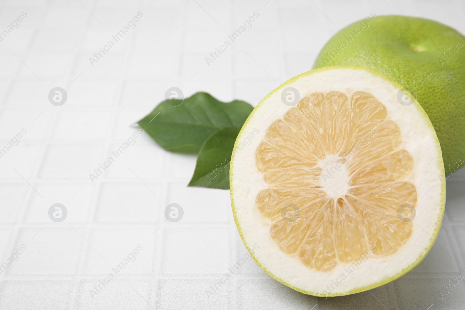 Photo of Whole and cut sweetie fruits with green leaves on white tiled table, closeup. Space for text