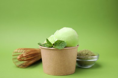 Photo of Paper cup with tasty matcha ice cream, bamboo whisk and powder on light green background