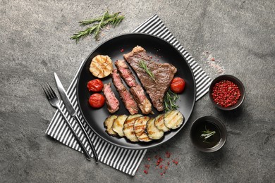 Photo of Delicious grilled beef steak with vegetables served on gray table, flat lay