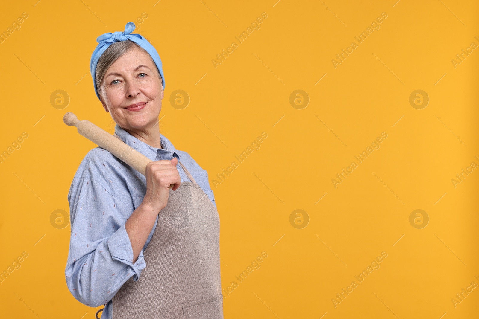 Photo of Happy housewife with rolling pin on orange background, space for text