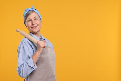 Photo of Happy housewife with rolling pin on orange background, space for text