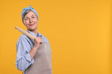 Happy housewife with rolling pin on orange background, space for text