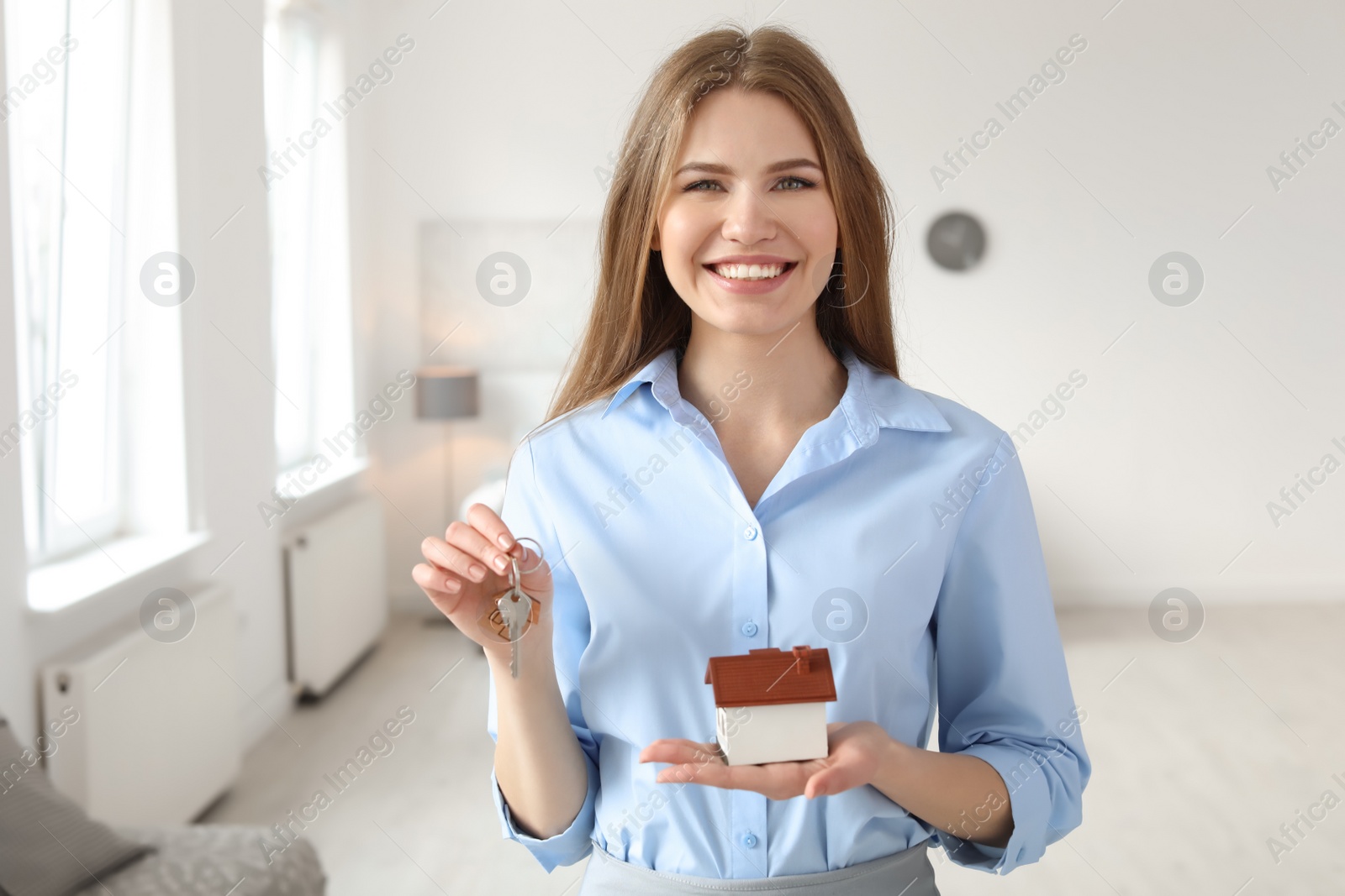 Photo of Beautiful real estate agent with house model and key indoors