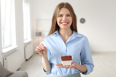 Beautiful real estate agent with house model and key indoors