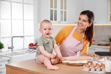 Happy young woman and her cute little baby cooking together in kitchen