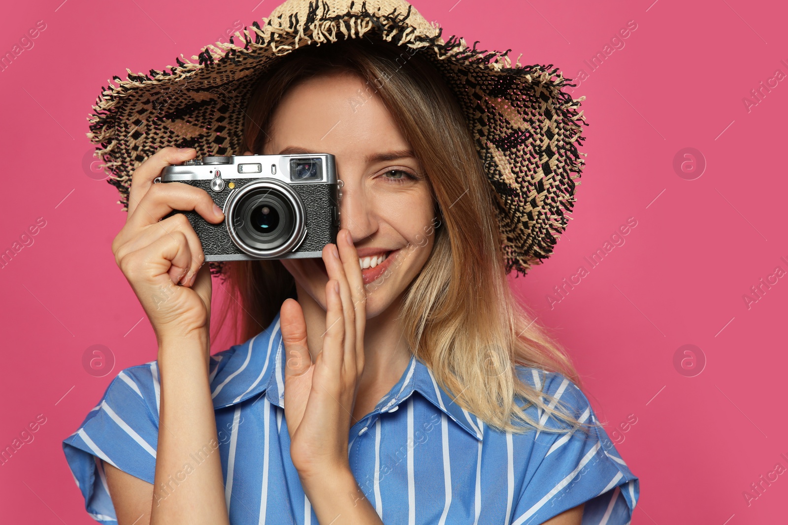 Photo of Beautiful young woman with straw hat and camera on crimson background. Stylish headdress