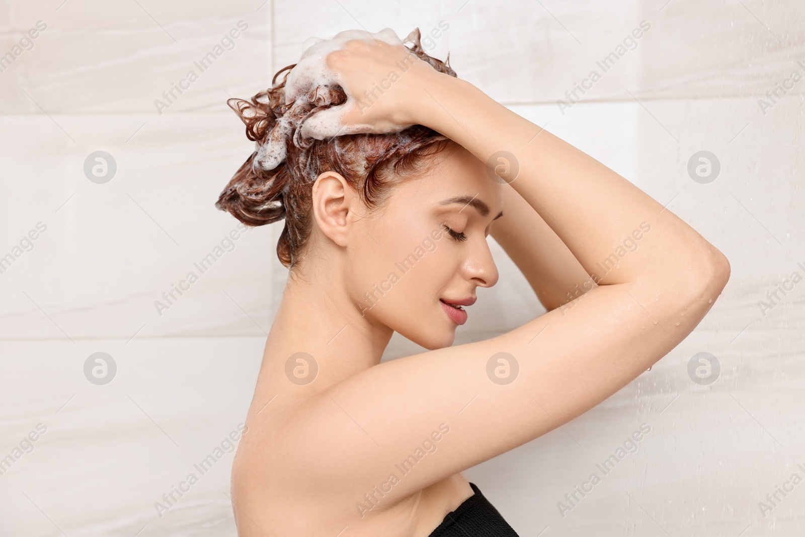 Photo of Young woman washing her hair with shampoo in shower
