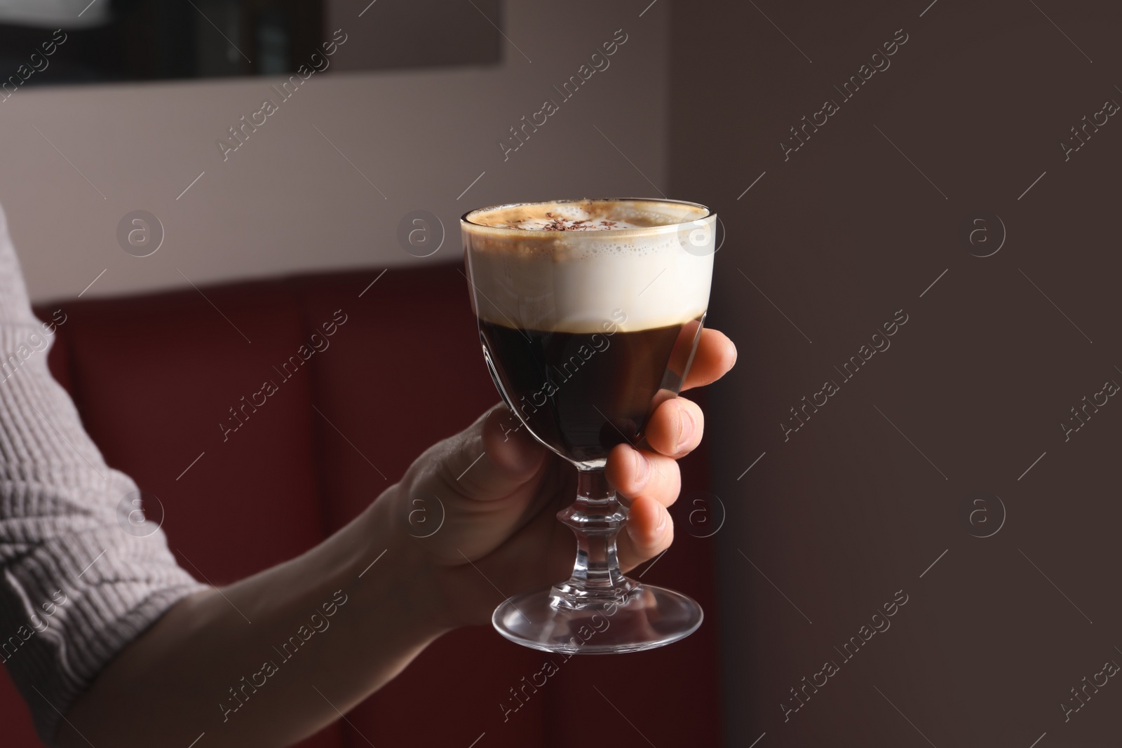 Photo of Woman holding glass of aromatic coffee drink with chocolate powder in cafe, closeup