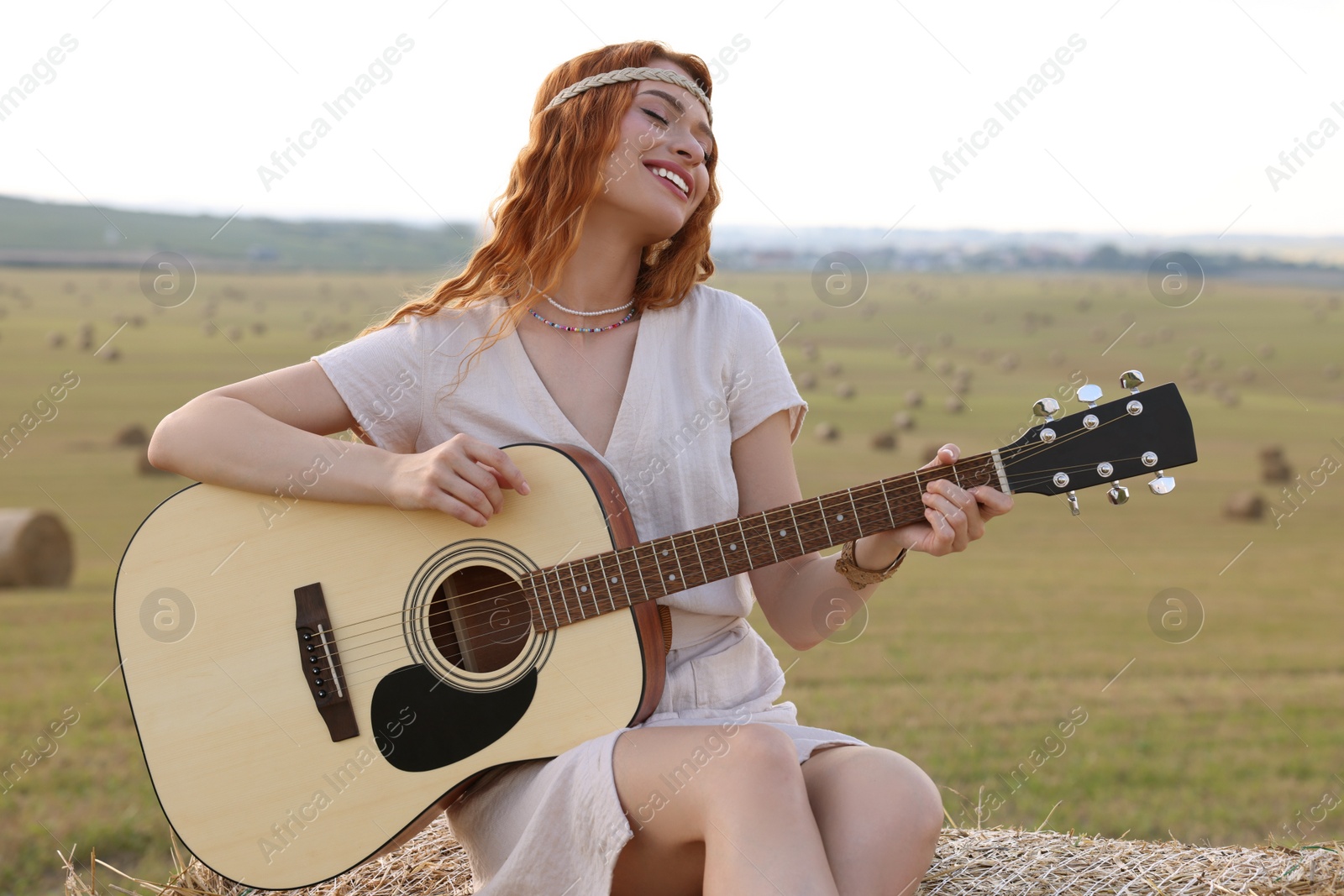 Photo of Beautiful hippie woman playing guitar on hay bale in field