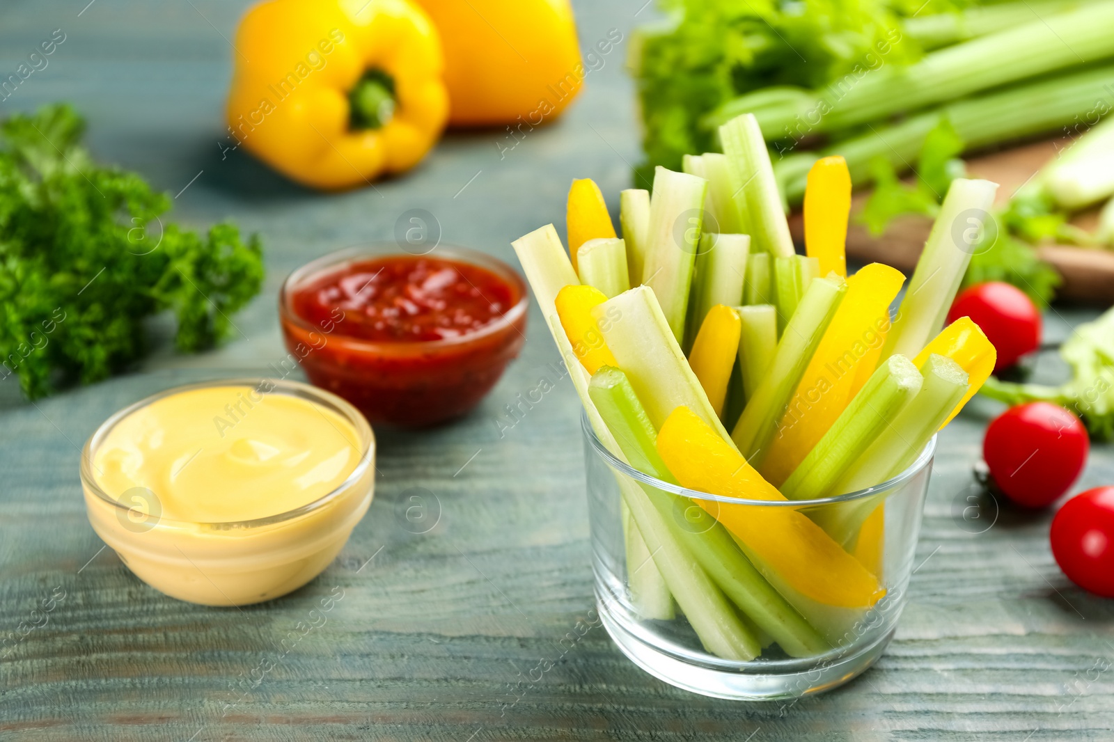 Photo of Celery sticks, pepper slices in glass bowl and different sauces on light blue wooden table