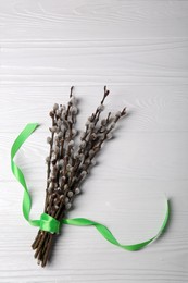Photo of Beautiful blooming willow branches with green ribbon on white wooden table, top view