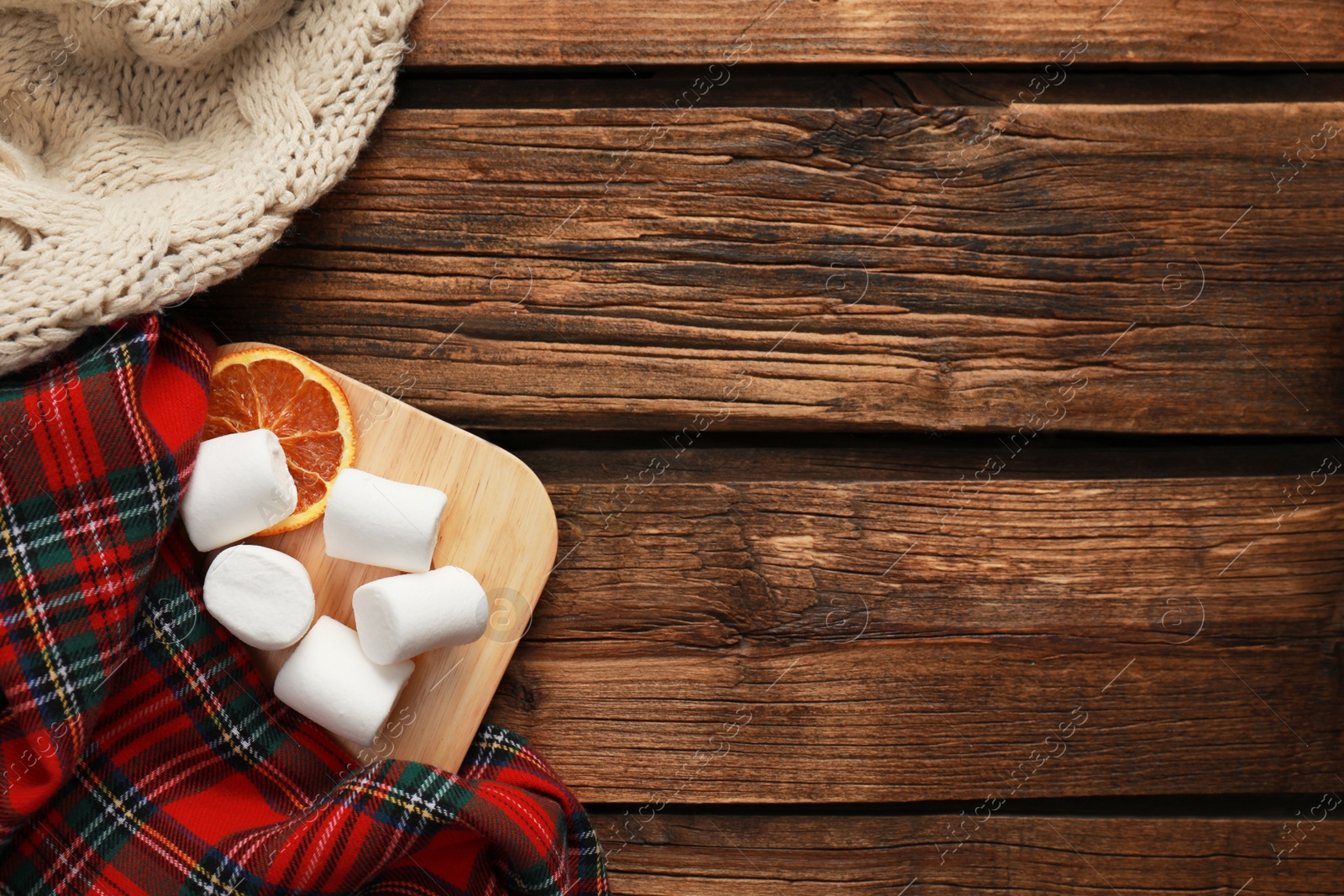 Photo of Flat lay composition with tasty marshmallows and warm blankets on wooden table, space for text. Cozy winter