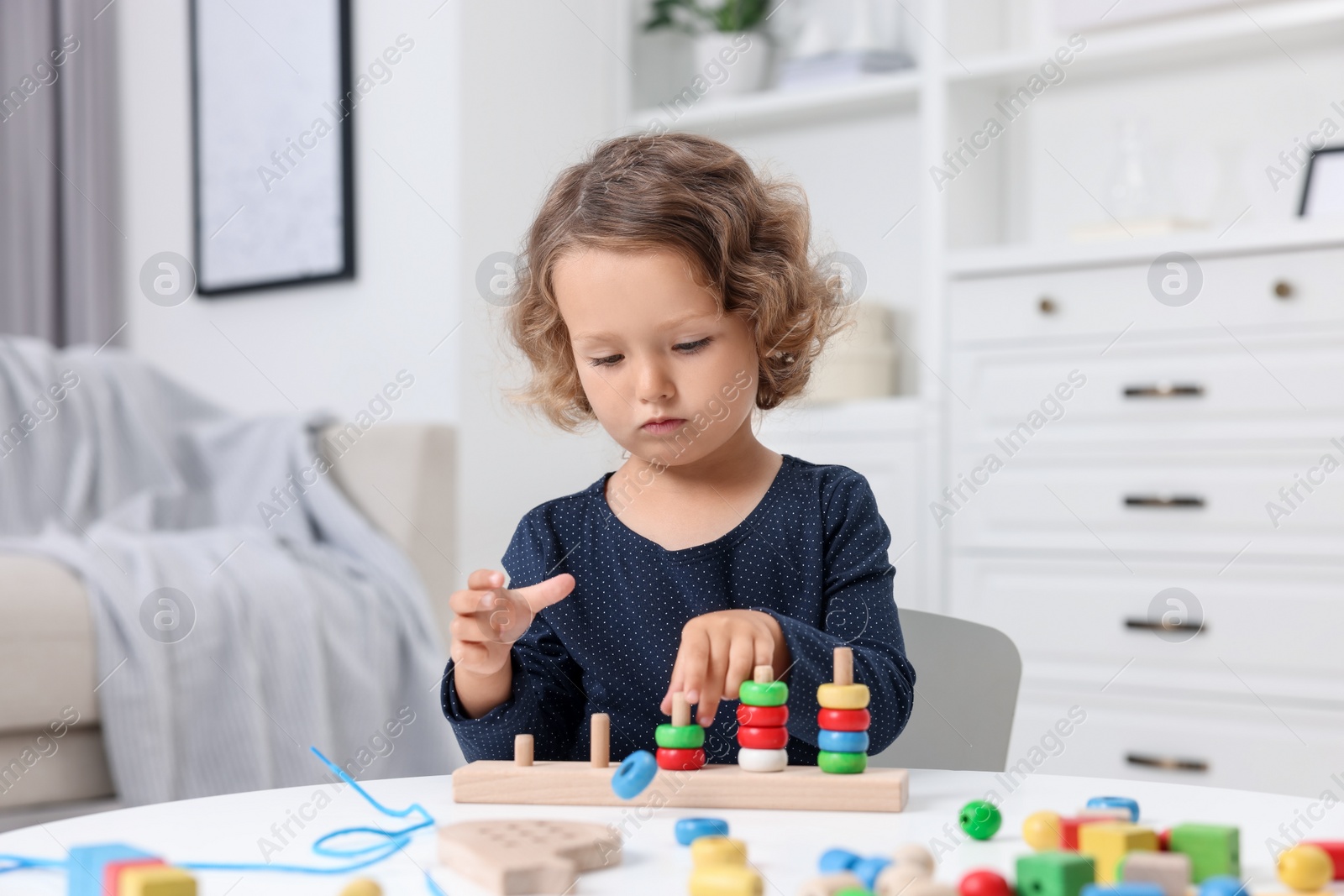 Photo of Motor skills development. Little girl playing with stacking and counting game at table indoors