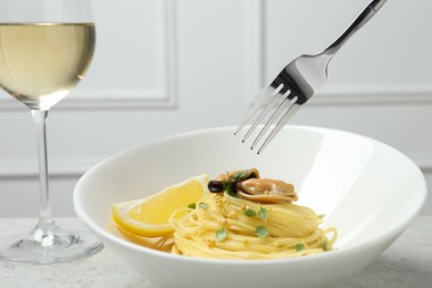Eating tasty capellini with mussels and lemon at light grey table, closeup. Exquisite presentation of pasta dish