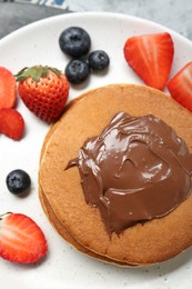 Photo of Tasty pancakes with chocolate paste and berries on plate, top view