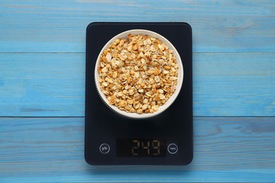 Photo of Digital kitchen scale with muesli on light blue wooden table, top view