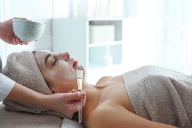 Cosmetologist applying mask on client's face in spa salon