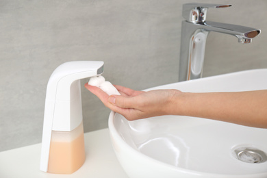 Woman using automatic soap dispenser in bathroom, closeup