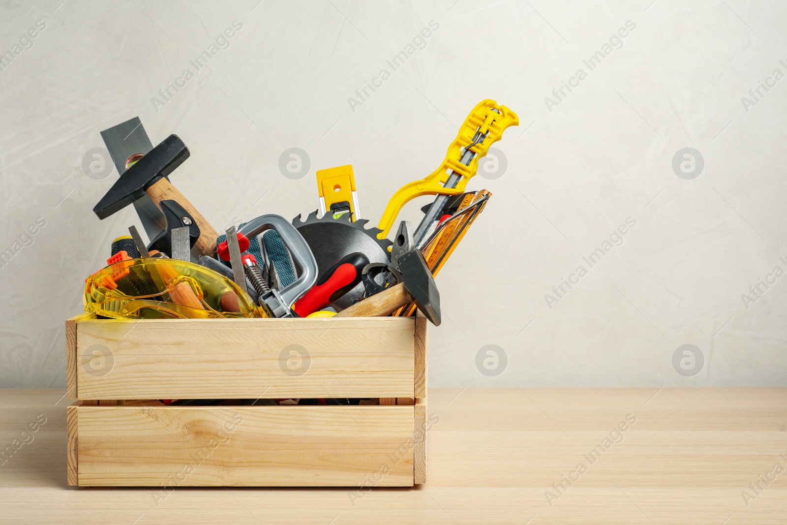 Photo of Crate with different carpenter's tools on wooden table. Space for text