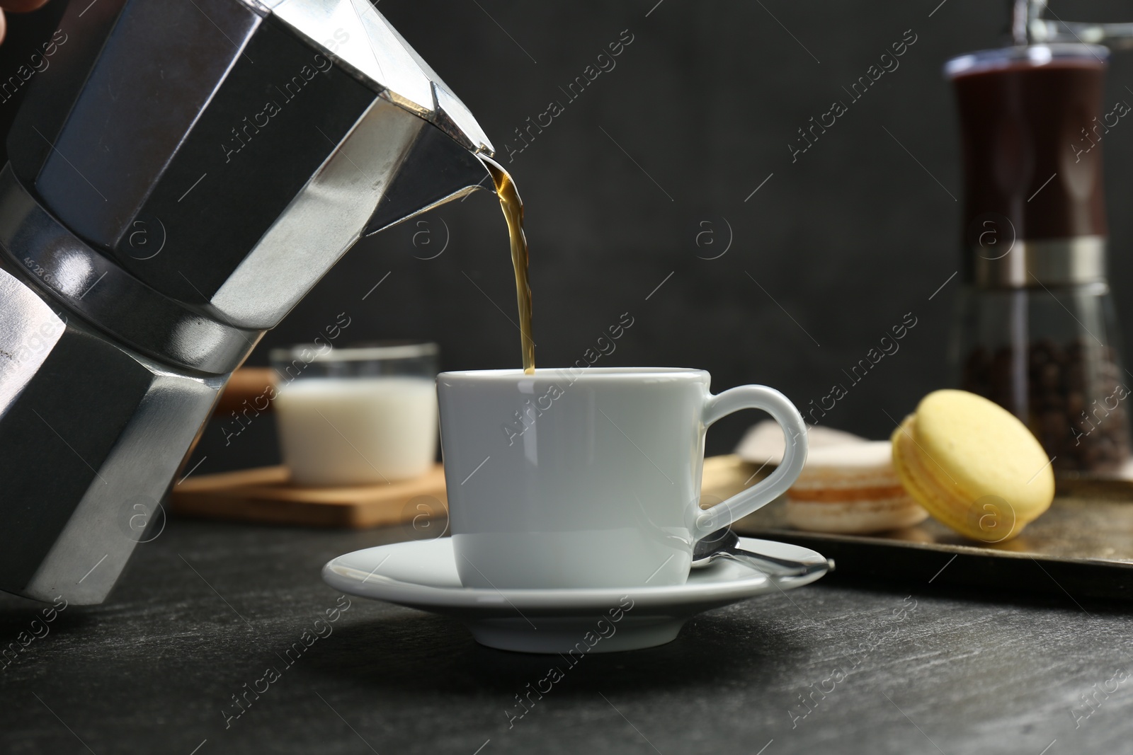 Photo of Pouring coffee from moka pot into cup at dark textured table, closeup
