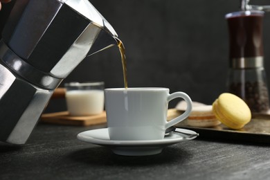 Pouring coffee from moka pot into cup at dark textured table, closeup