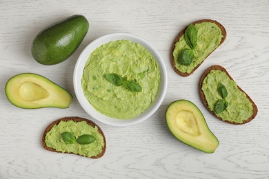 Flat lay composition with guacamole, sandwiches and avocados on white wooden table